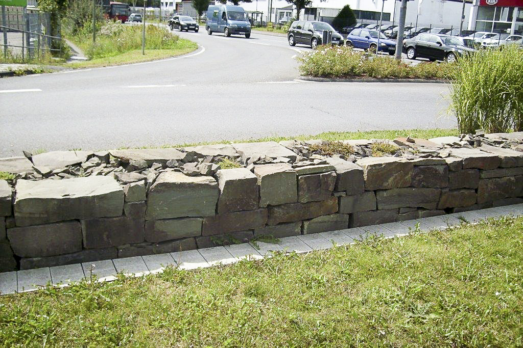 Bepflanzte Natursteinmauer an einer Straßenböschung